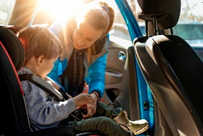 Toddler being buckled in car seat by mom